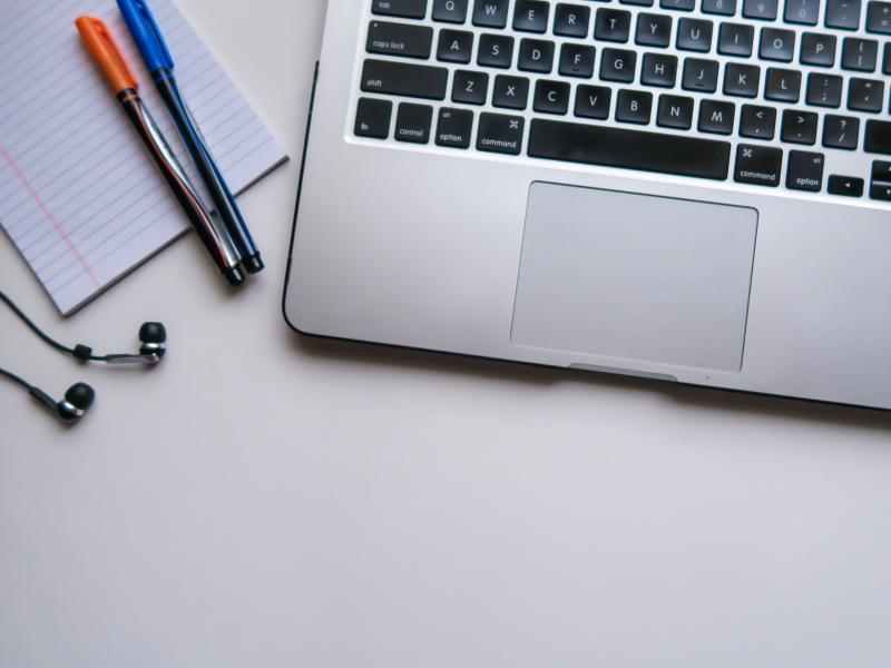 A laptop, two pens, a notepad and headphones are laying on a table