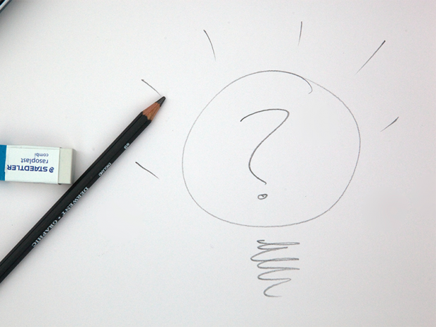 A pencil and rubber lying on a piece of paper next to a drawing of a lightbulb with a question mark in the centre 