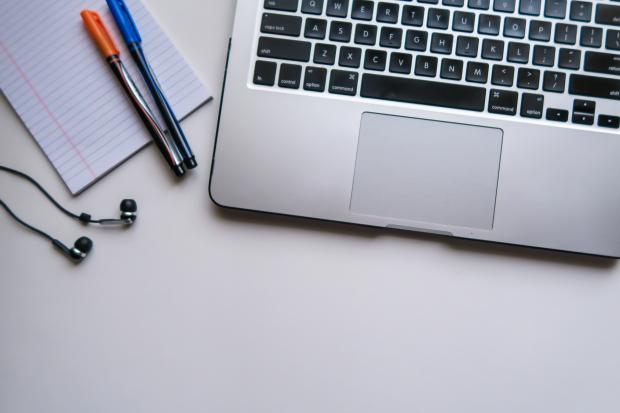 A laptop, two pens, a notepad and headphones are laying on a table