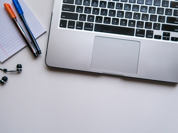 A laptop, two pens, a notepad and headphones are laying on a table